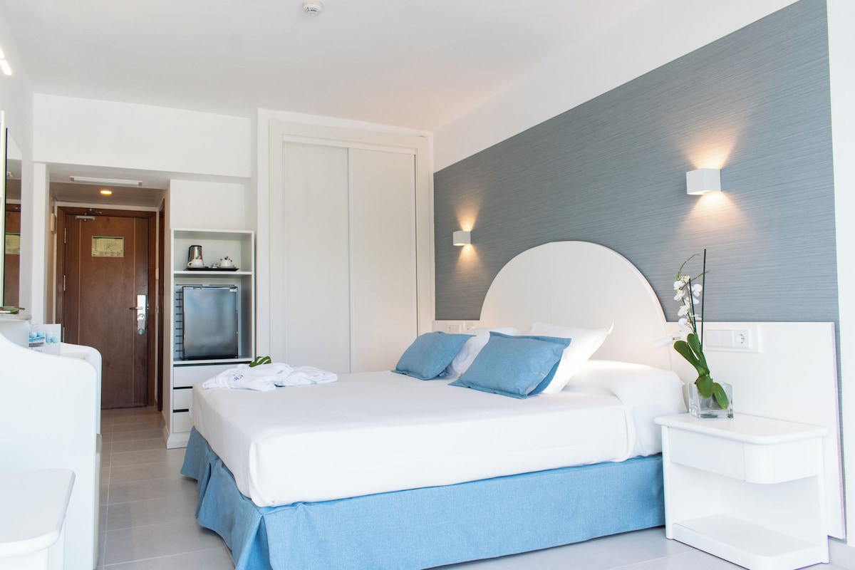 A modern hotel room with a large bed, a bedside table, a built-in TV, and a bathroom visible through an open door.