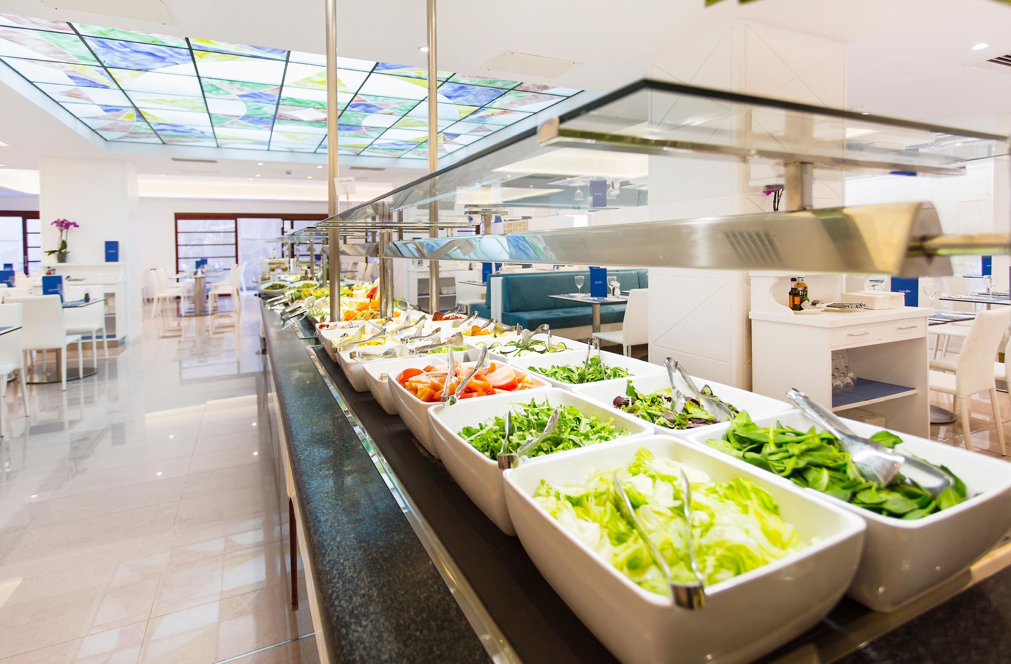 Un bufé con diversas opciones de comida, techo de vidrio y un interior moderno y luminoso.