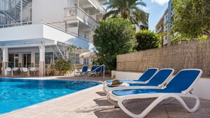 A poolside area with lounge chairs, a pool, and a building with balconies. - BLUESEA Piscis (Alcúdia)