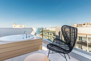 A balcony with a bathtub, a wicker chair, and a view of the city. - Hotel Cabot Playa Grande - Adults Only (Palma de Mallorca)