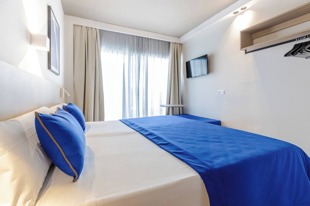 A hotel room with a bed, a TV mounted on the wall, and a window with curtains.