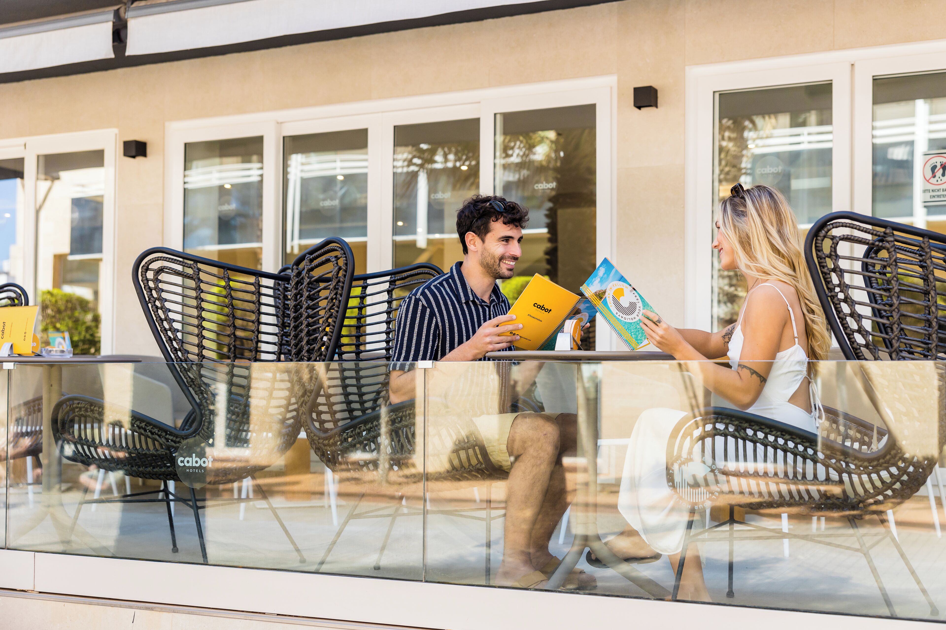 Un café con terraza, que incluye sillas de mimbre y una mesa de vidrio.