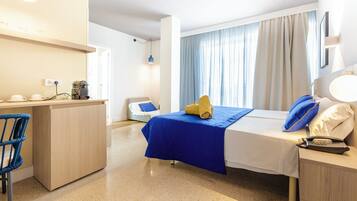 Una habitación de hotel con cama, mesita de noche, escritorio, silla y ventana con cortinas.