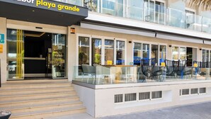 A modern building with a glass facade, a sign reading "cabot playa grande," and outdoor seating with chairs and tables. - Hotel Cabot Playa Grande - Adults Only (Palma de Mallorca)