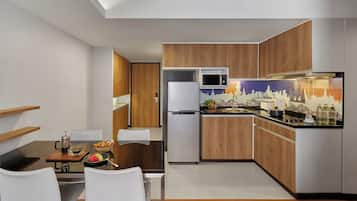 A modern kitchen with wooden cabinets, a white refrigerator, a microwave, and a dining area with a table and chairs.