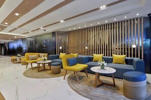 Un vestíbulo moderno con una zona de estar que incluye sofás y sillones, una mesa de centro redonda y una pared decorativa con listones de madera verticales.