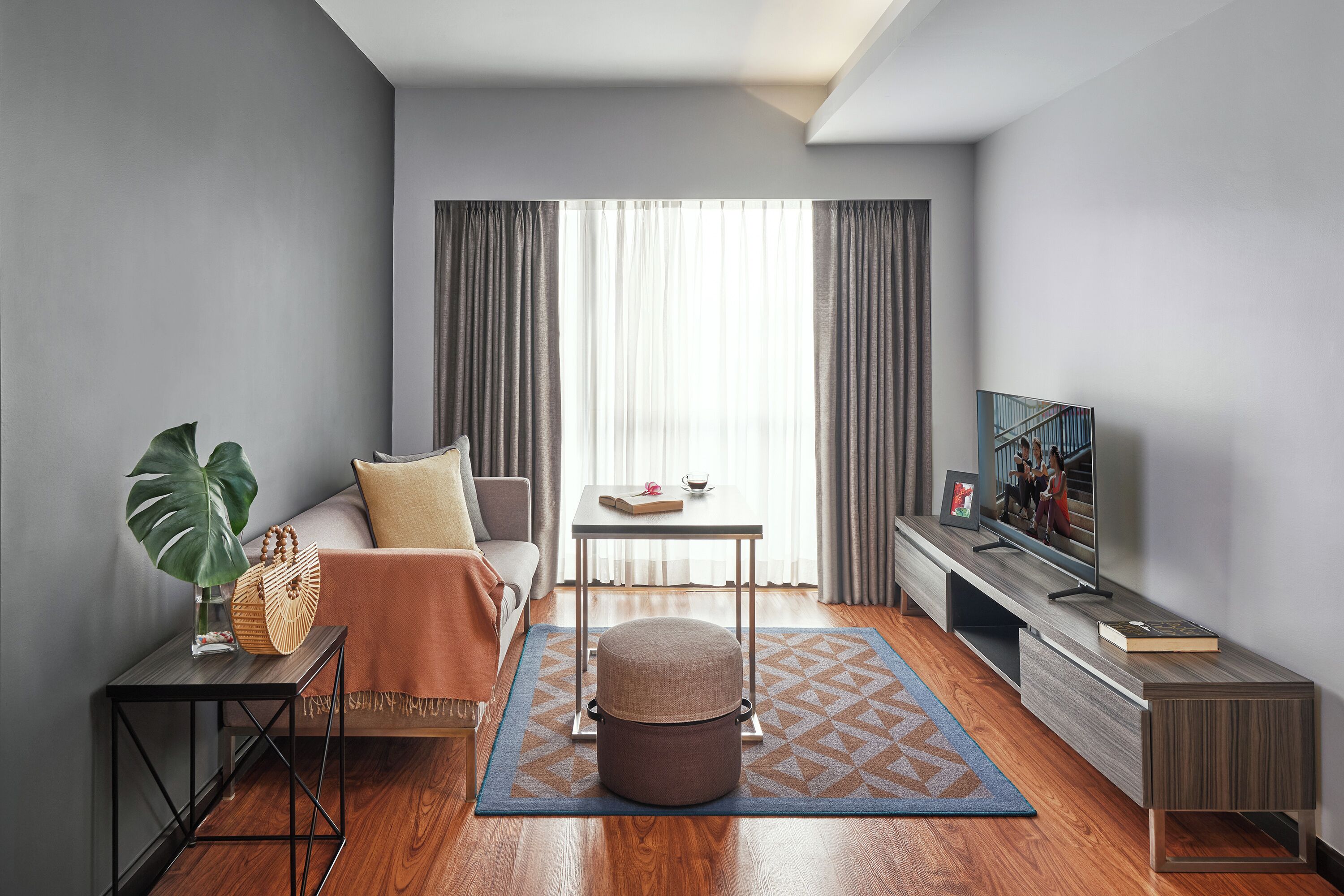 A modern living room with a sofa, ottoman, coffee table, TV, and a large window with curtains.