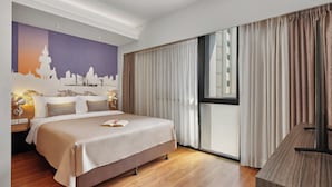 Une chambre d’hôtel avec un lit, un bureau, une grande fenêtre avec des rideaux et une fresque représentant un paysage urbain sur le mur.