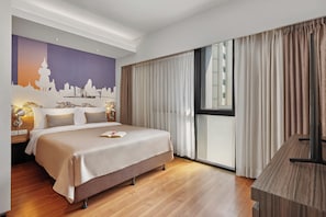 Ein Hotelzimmer mit Bett, Schreibtisch, großem Fenster mit Vorhängen und Wandgemälde mit Stadtansicht.