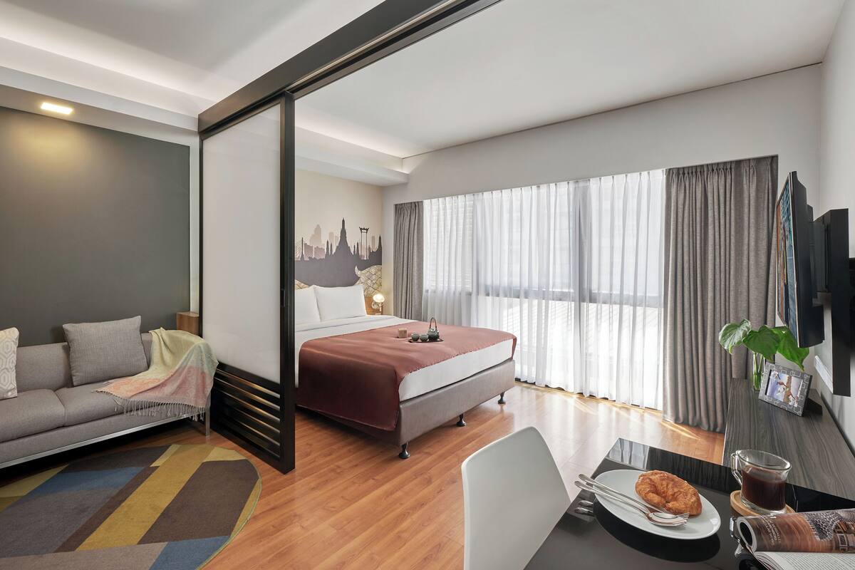 Une chambre d’hôtel moderne équipée d’un lit, d’un canapé, d’une table à manger et d’une grande fenêtre avec des rideaux.