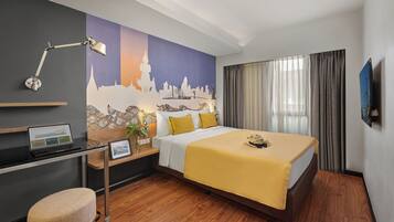 Une chambre d’hôtel avec un lit, un bureau, un ordinateur portable et une fresque représentant un paysage urbain sur le mur.