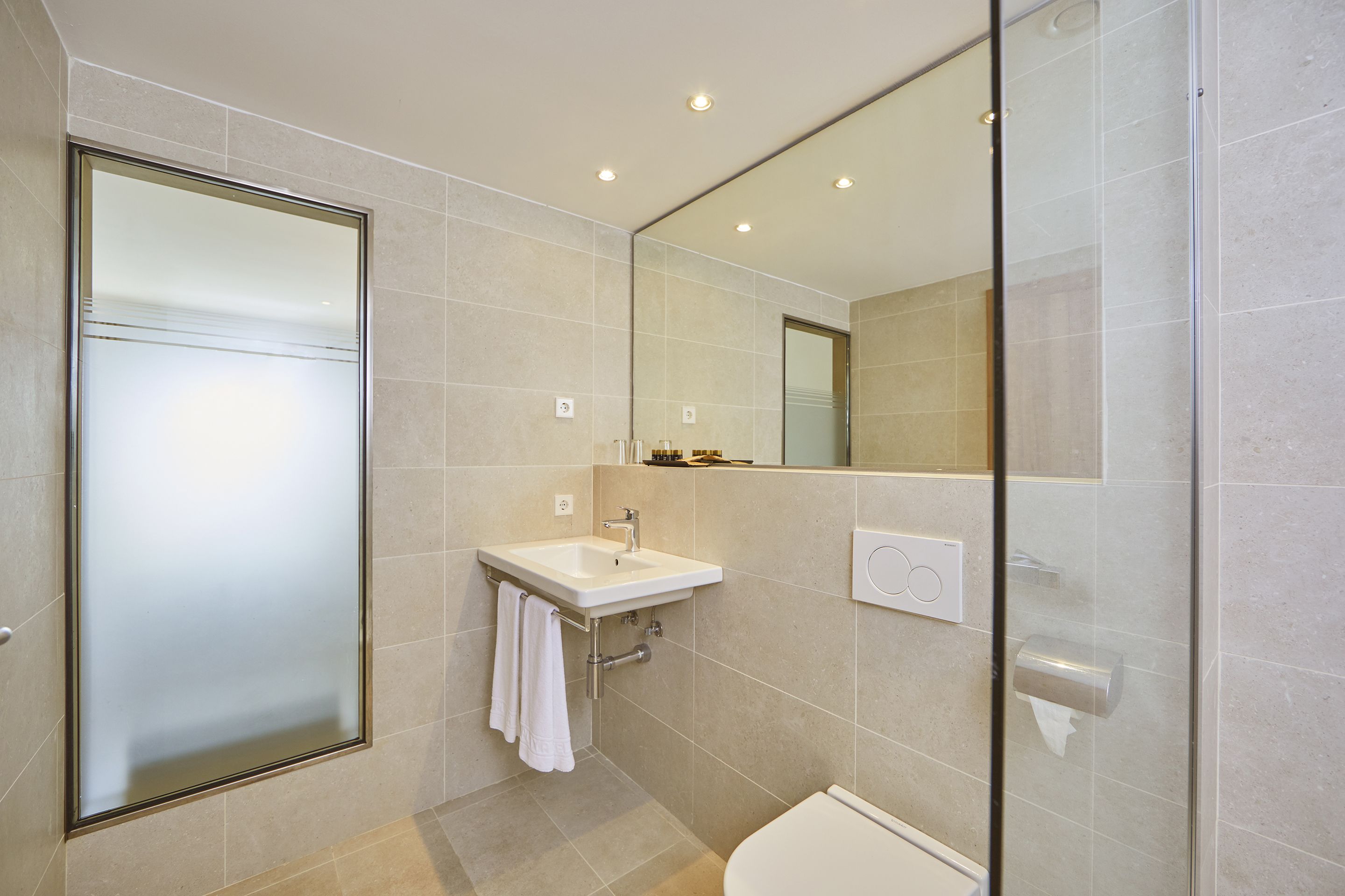 A modern bathroom with a glass shower enclosure, a sink with a towel, and a toilet.