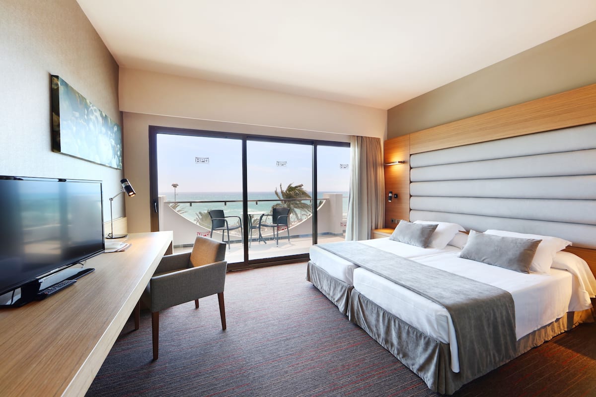 Une chambre d’hôtel avec un grand lit, un bureau avec une télévision et un balcon offrant une vue sur l’océan.