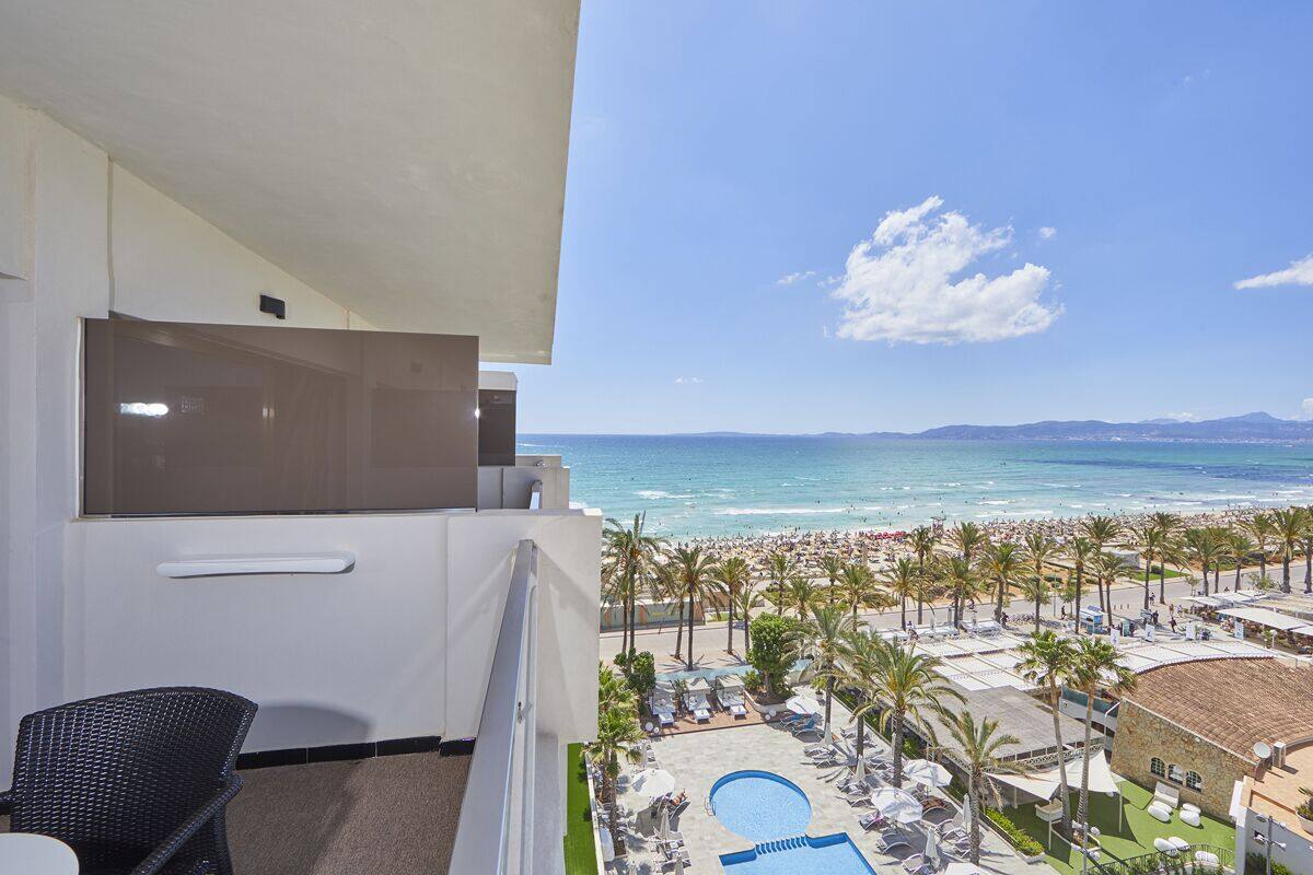 Un balcon avec vue sur une plage, une piscine et des palmiers.