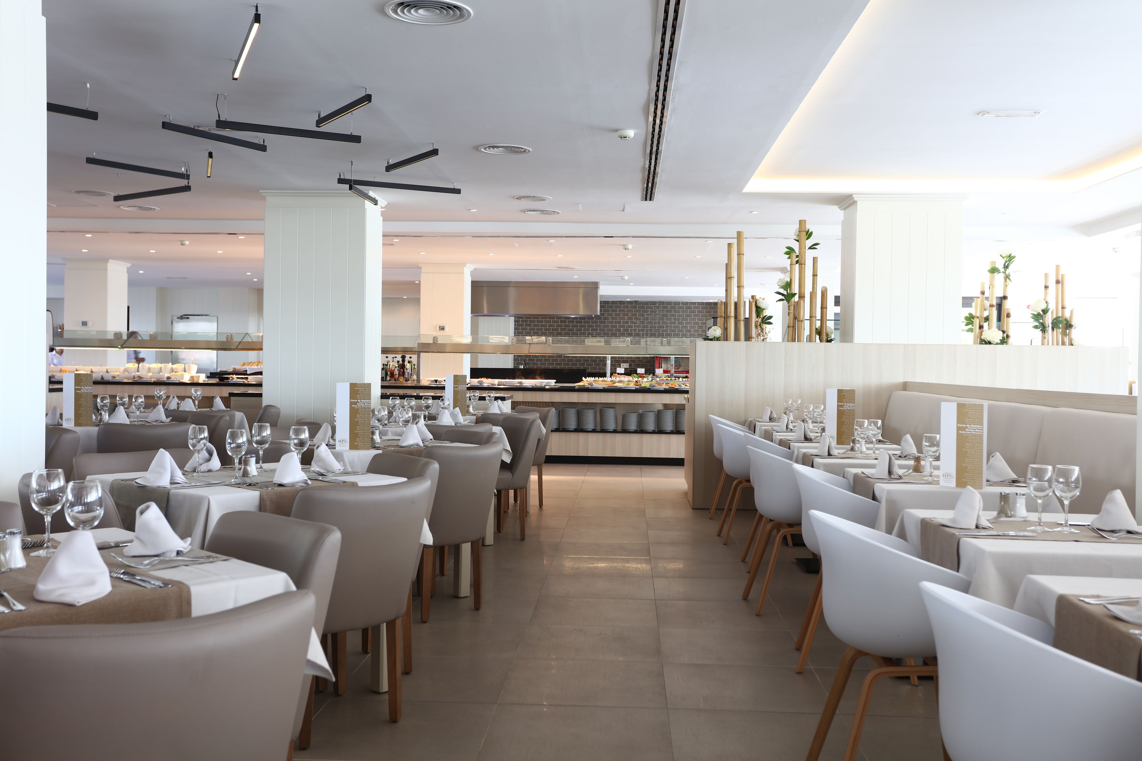 Un restaurant moderne doté de plusieurs tables, de chaises blanches et d’un espace cuisine central.