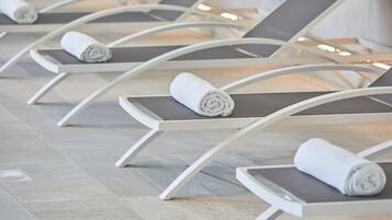 A row of white lounge chairs with grey cushions and rolled white towels placed on them.