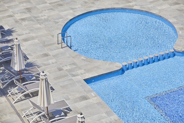 Una piscina con solárium empedrado, sillas de descanso y sombrillas.