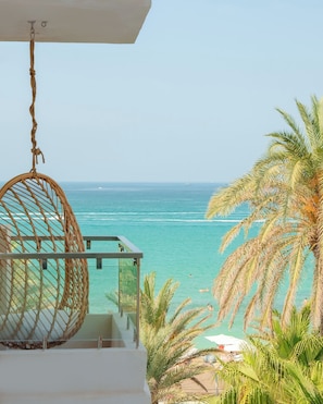 Un balcón con una hamaca de mimbre con vistas a aguas turquesas y palmeras.