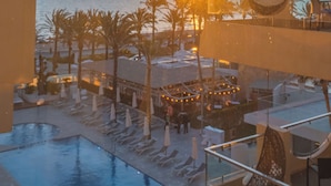 Un área de piscina en la azotea con sillones de descanso, una silla colgante y vistas a la puesta de sol sobre el océano.