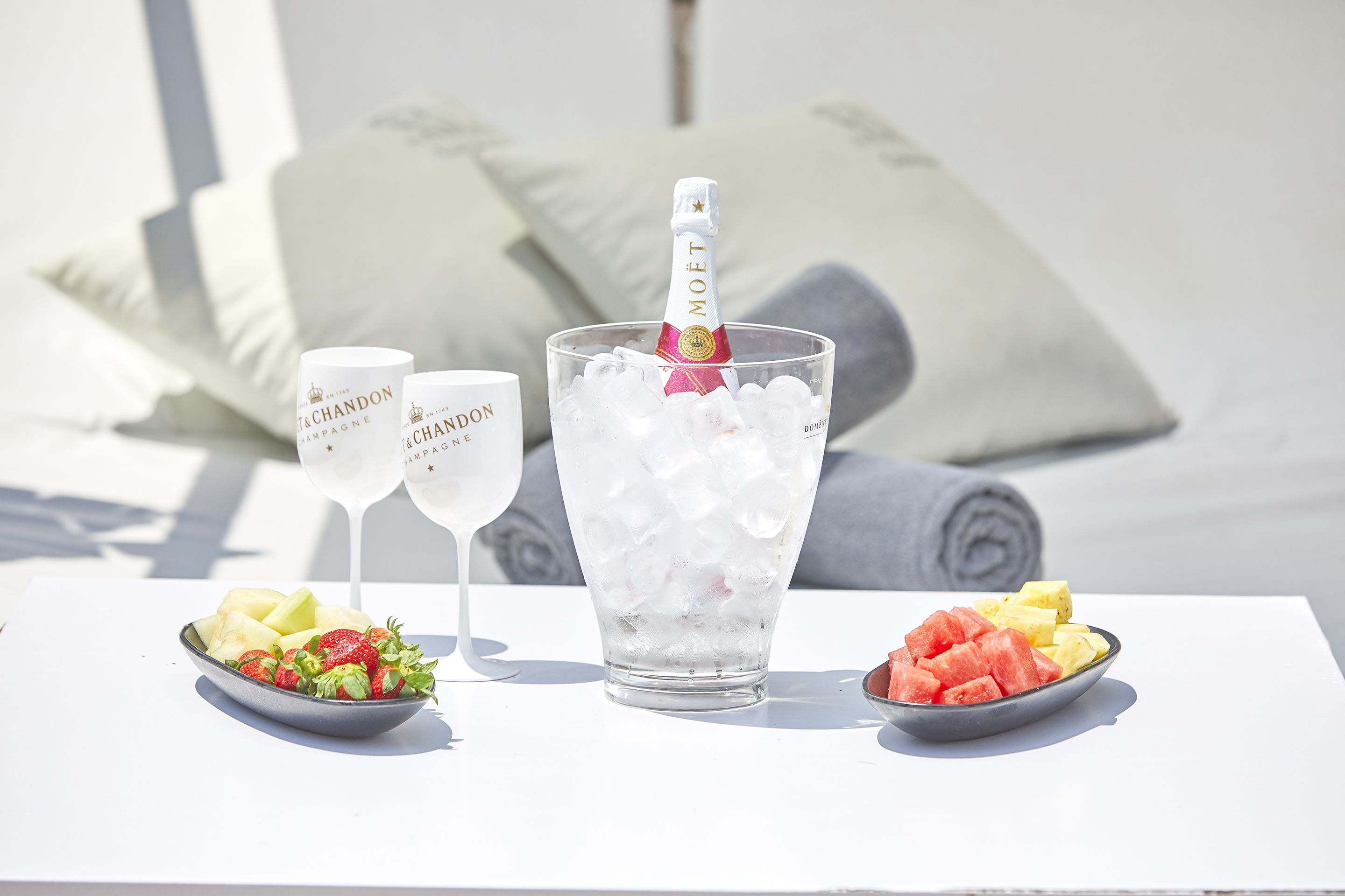 A table with a bottle of champagne, two glasses, and bowls of fruit.