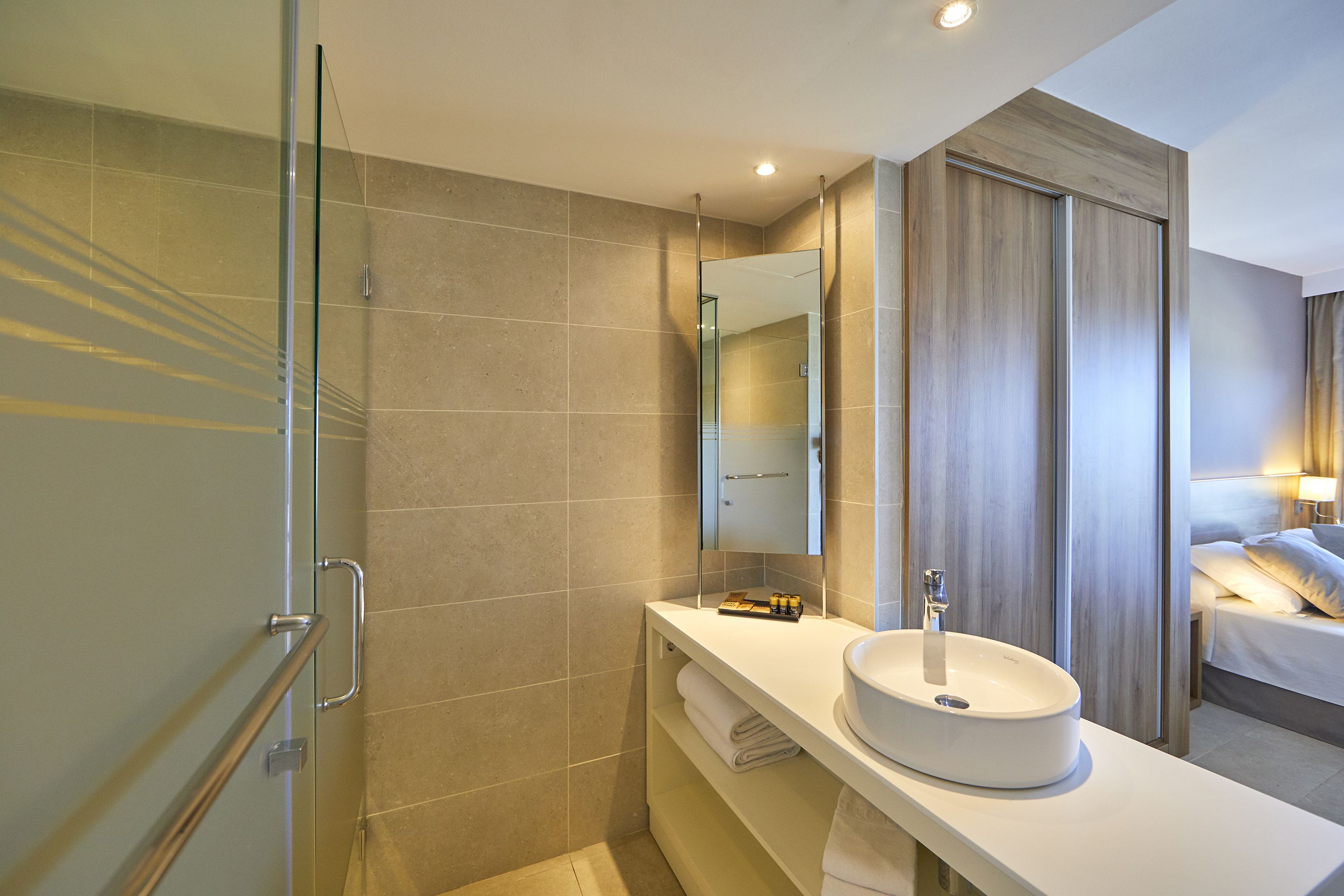 Une salle de bain moderne avec une douche à l’italienne en verre, un lavabo blanc et un grand miroir.