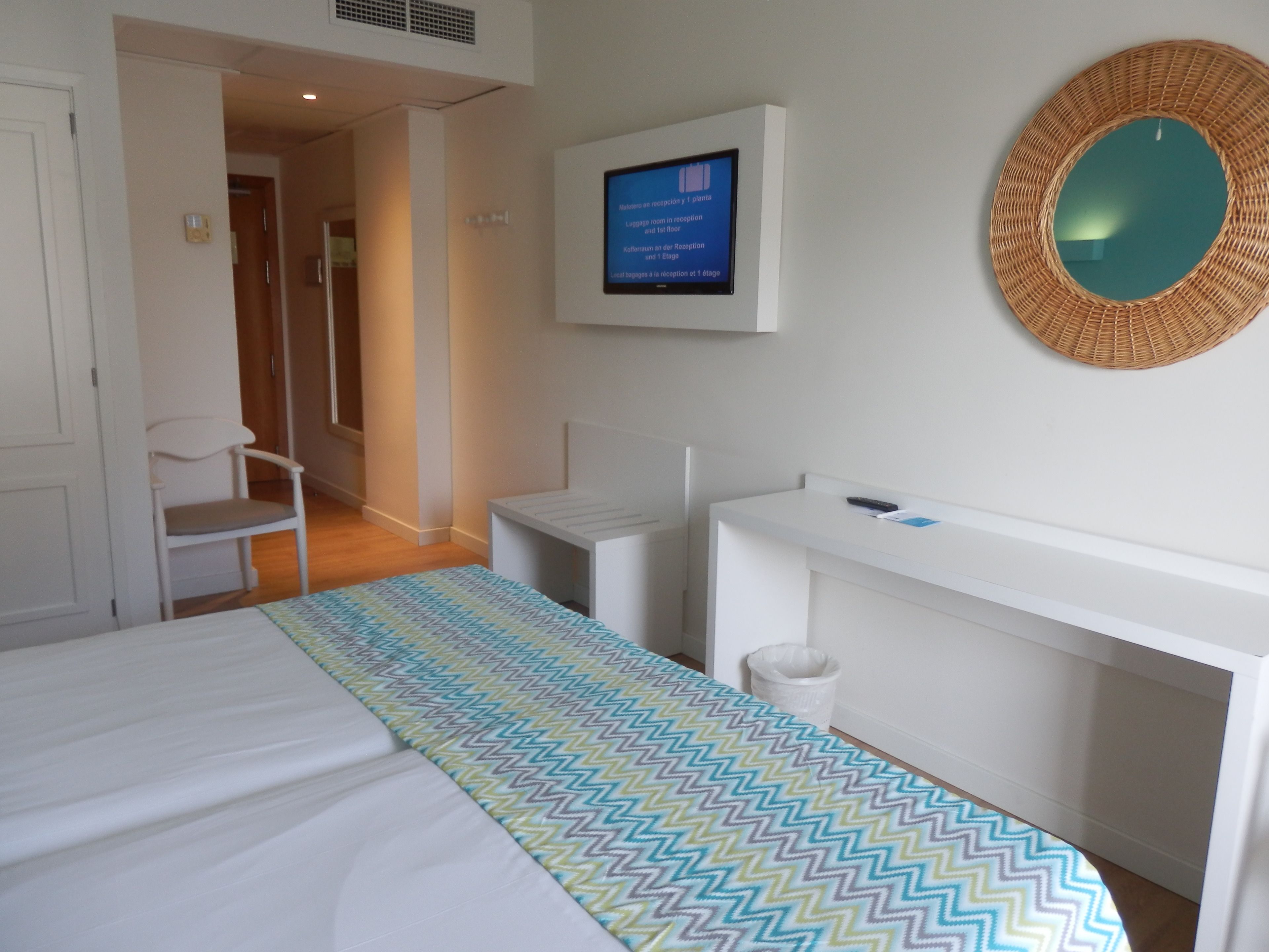 A hotel room with a bed, a desk, a chair, a television, and a mirror.
