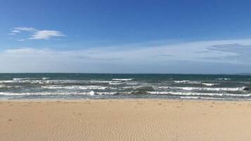 A sandy beach with waves approaching the shore under a clear sky.
