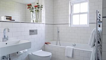 A modern bathroom with white tiles, a white sink, a toilet, a bathtub, and a window.
