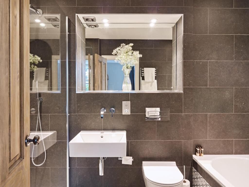 A modern bathroom with a large mirror, a white sink, a toilet, and a bathtub.