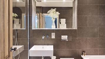 A modern bathroom with a large mirror, a white sink, a toilet, and a bathtub.