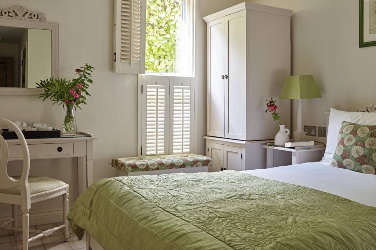 Une chambre à coucher comprenant un lit, un bureau, une chaise, une armoire, une fenêtre avec des volets et une table de chevet avec une lampe.