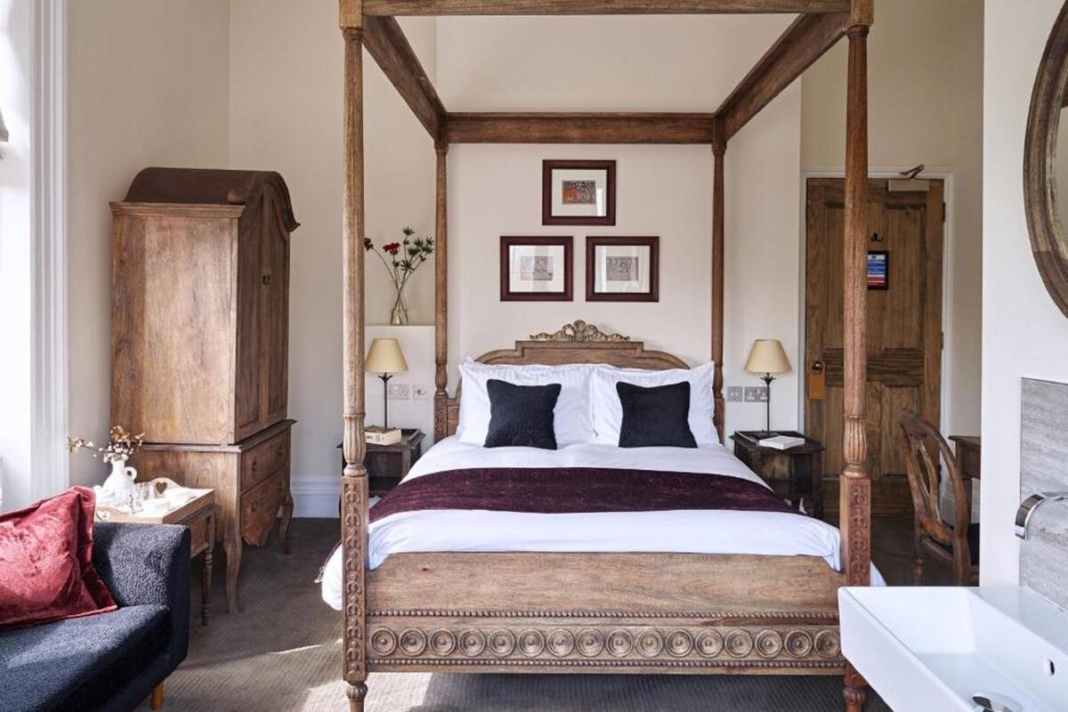 Un lit à baldaquin avec un cadre en bois, une table de chevet avec une lampe, une armoire en bois et un miroir au mur.