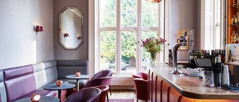A bar area with a bar counter, seating with round tables, and a large window with a view of greenery.