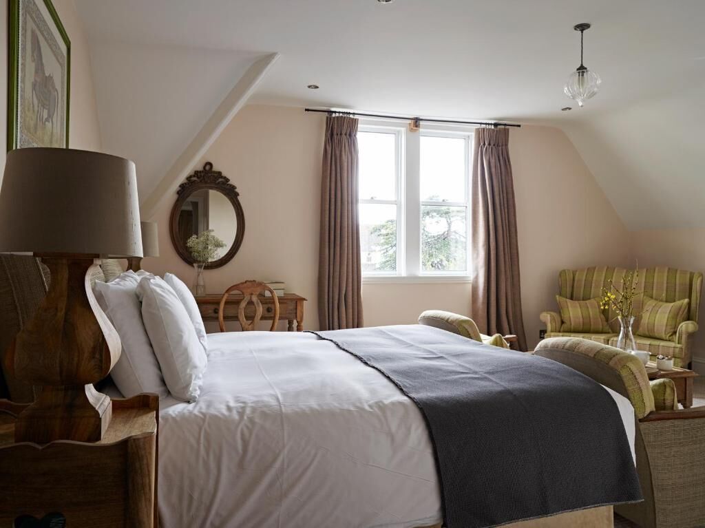 A bedroom with a large bed, a wooden nightstand, a chair, and a window with curtains.