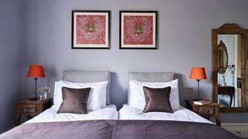 Cama doble con sábanas blancas y dos almohadas, flanqueada por mesitas de noche con lámparas, en una habitación con un espejo grande y dos obras de arte enmarcadas en la pared.