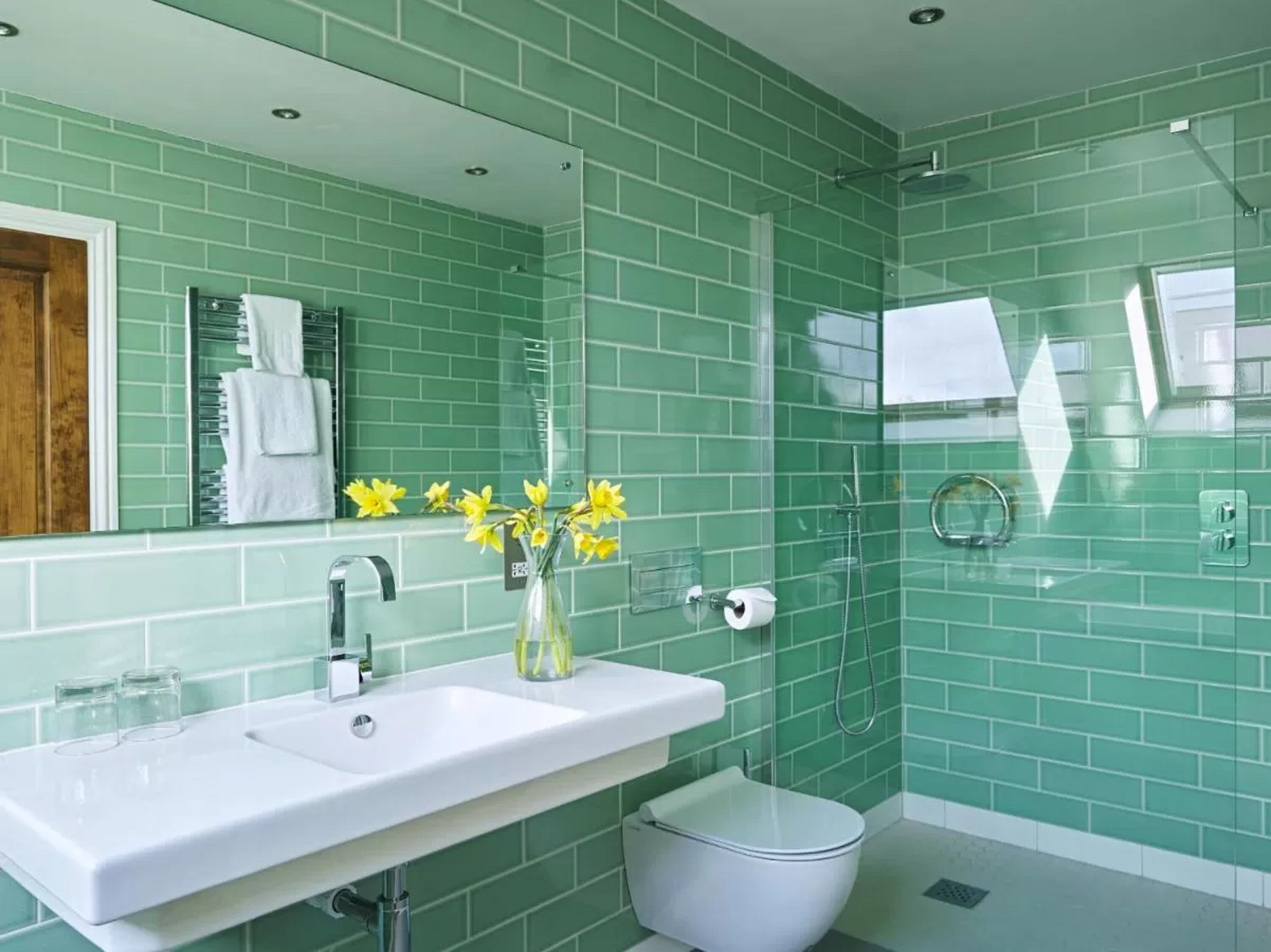 Un baño con lavamanos blanco, cabina de ducha con mampara de vidrio y paredes con azulejos verdes.