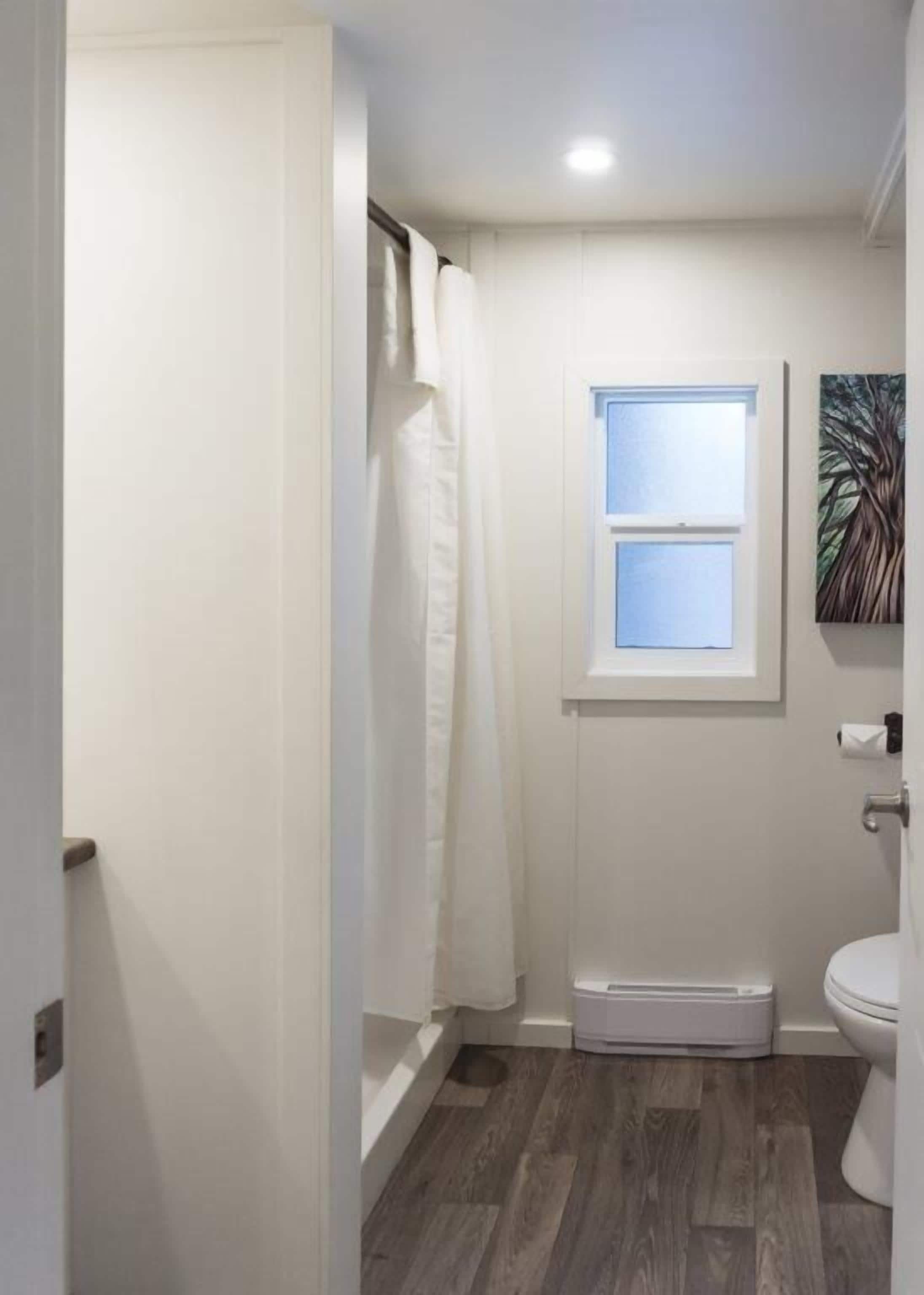 Een badkamer met een douche, een raam, een toilet en een klein wastafeltje.