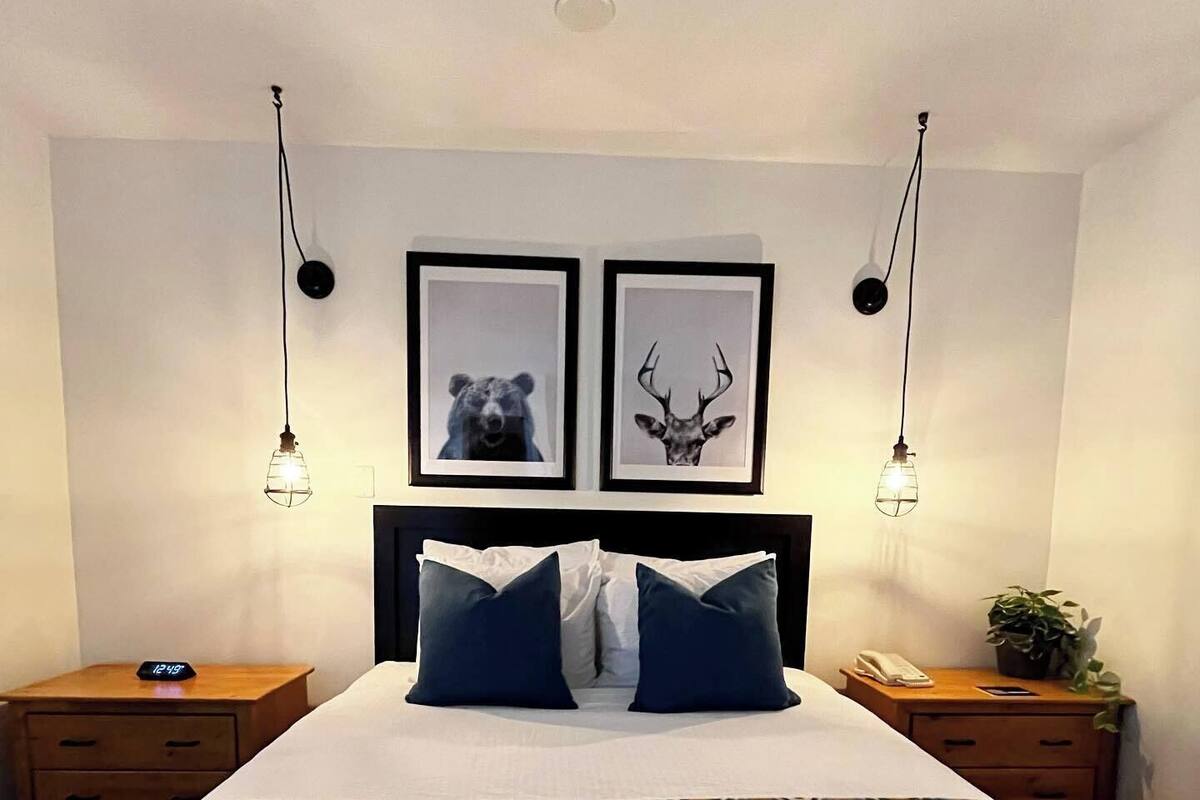 A bedroom with a bed, two nightstands, a clock, and two framed pictures on the wall.