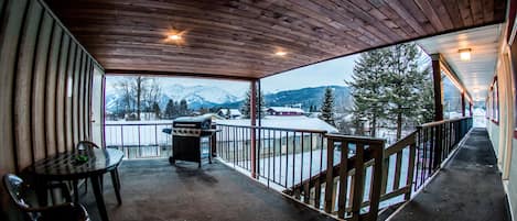 A covered balcony with a view of snow-covered mountains and a grill.