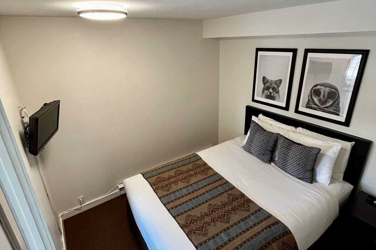 A hotel room with a bed, a flat-screen TV mounted on the wall, and two framed pictures above the bed.