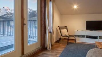 A room with a large sliding glass door leading to a snowy outdoor area, a television on a white cabinet, and a chair.