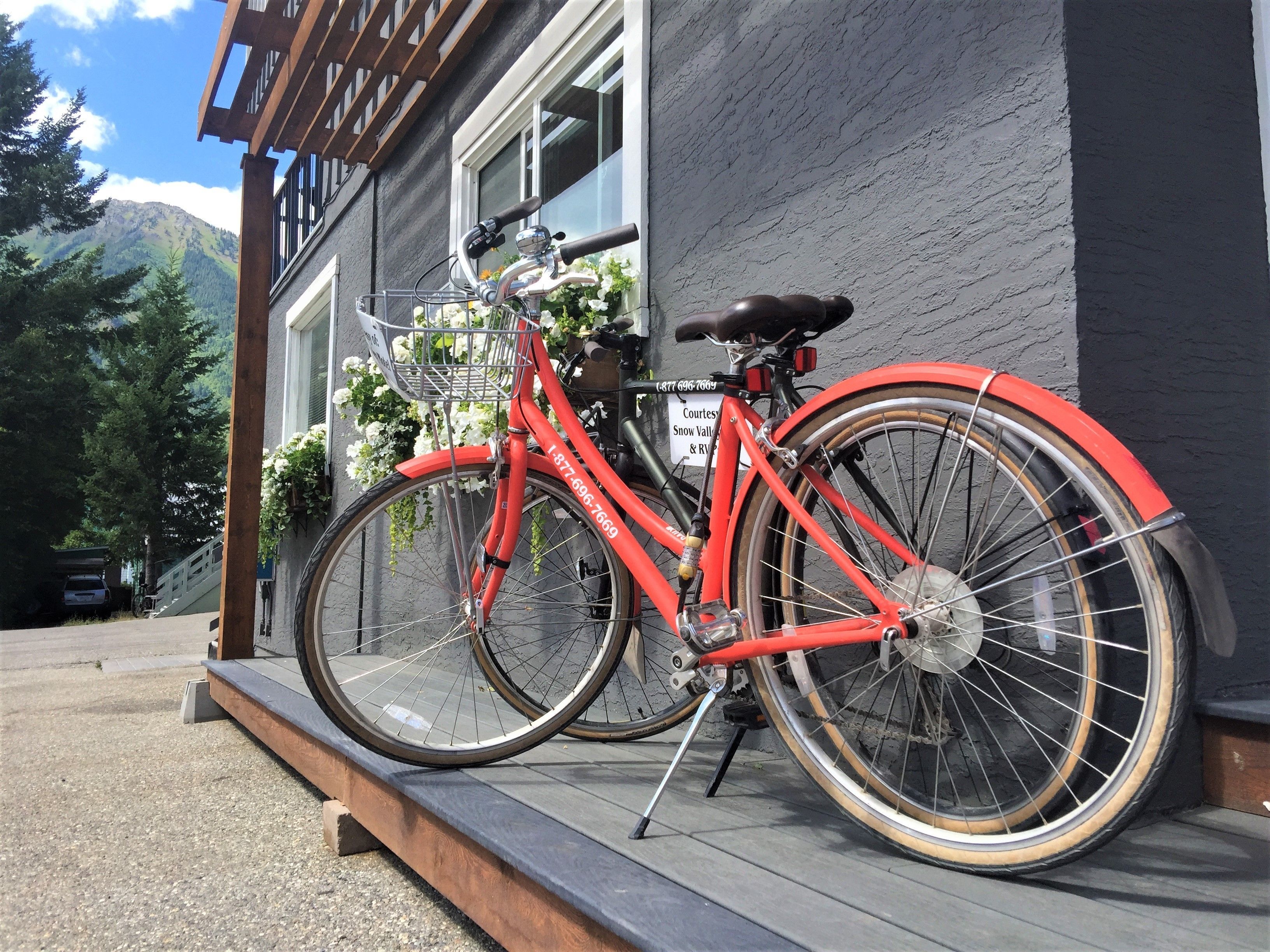 A red bicycle parked on a wooden platform in front of a building with a mountain view.