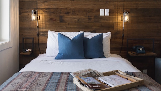 A neatly made bed with blue and white pillows, a wooden headboard, and a tray with reading materials on a patterned bedspread. - Snow Valley Lodging (Fernie)