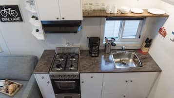 Una kitchenette compacta con estufa a gas, horno y lavabo, armarios blancos y una ventana sobre el lavabo.