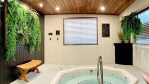 A hot tub with a wooden bench, surrounded by potted plants and a window with blinds. - Snow Valley Lodging (Fernie)