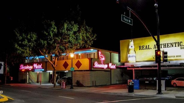A hotel with neon signs, a street sign, and a traffic light.