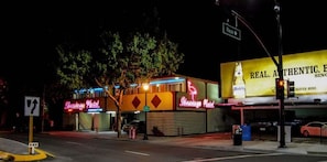A hotel with neon signs, a street sign, and a traffic light.