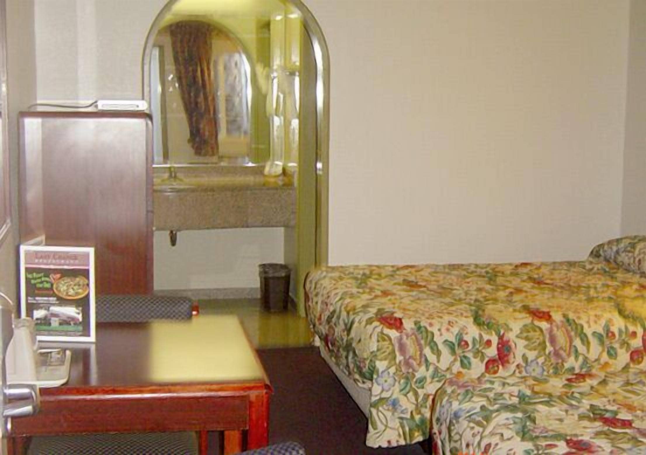 Hotellihuone, jossa on sänky, työpöytä, tuoli, pieni pöytä ja peili.