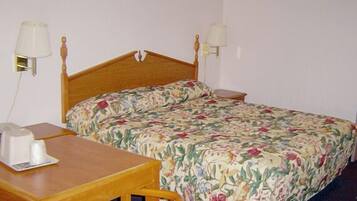 A single bed with a floral bedspread, a wooden nightstand, a bedside table with a lamp, and a wall-mounted lamp.