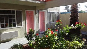A two-story building with a balcony, a red door, and a small garden with red flowers.